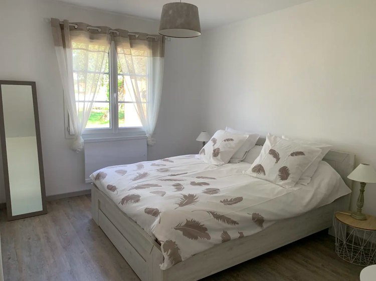Chambre avec lit double, décoration sobre et fenêtre donnant sur le jardin à Oléron.